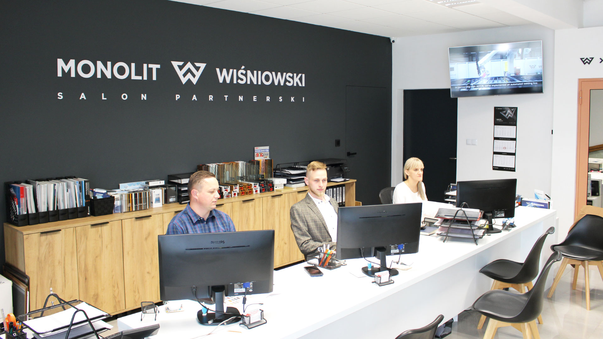 Jesteśmy salonem partnerskim Wiśniowski. Na zdjęciu widoczni są pracownicy salonu firmowego Monolit: Aneta, Maciej i Krzysztof, siedzący przy biurku.