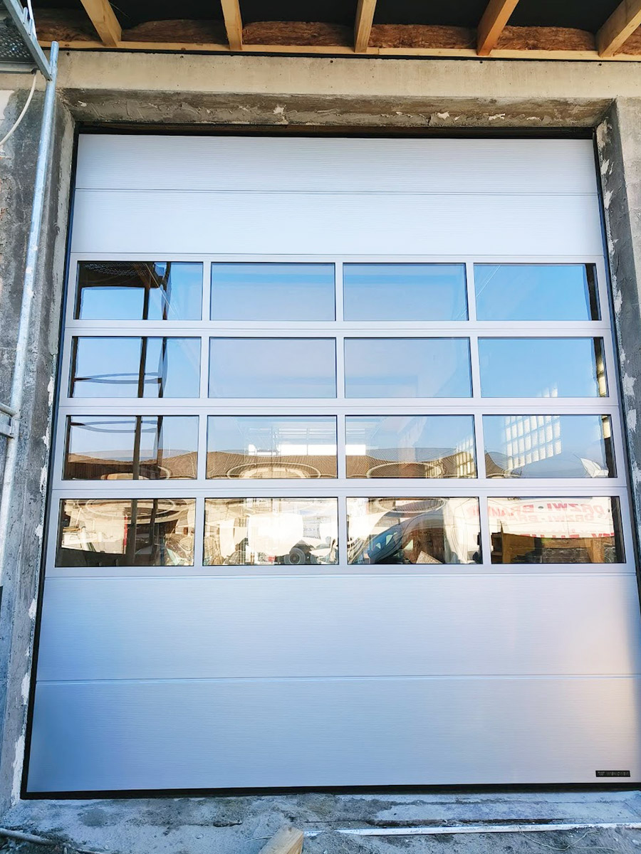 Zdjęcie przedstawiające bramą segmentową z oknami z zewnątrz. Montaż wykonała firma Monolit Spółka Jawna Zawada.