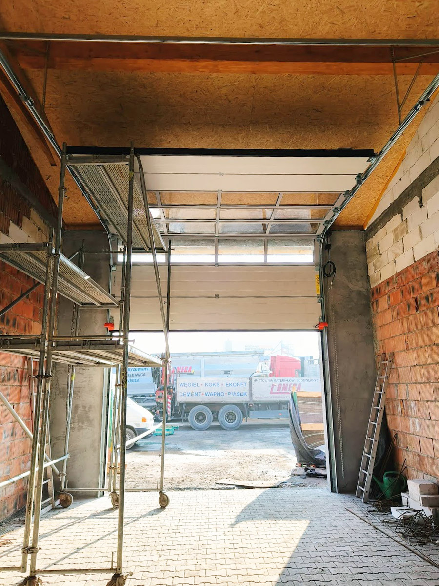 Zdjęcie przedstawiające wnętrze garażu z bramą segmentową z oknami podczas montażu. Realizację wykonała firma Monolit Spółka Jawna Zawada.