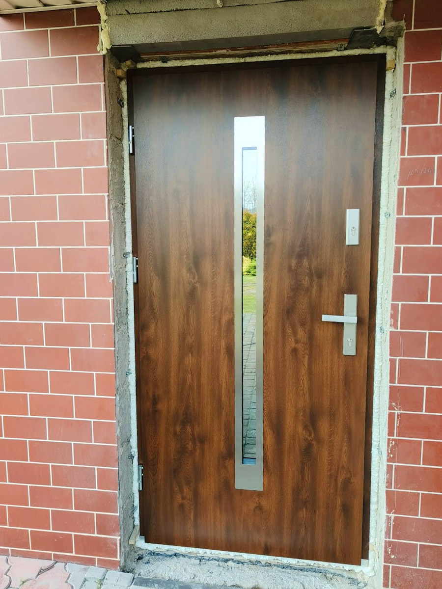 Zdjęcie przedstawiające drzwi zewnętrzne koloru drewnopodobnego ciemnego. Montaż wykonała firma Monolit Spółka Jawna Zawada.